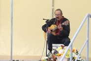Aleksandr Maceradi siedzi na tarasie SCK zameczek, gra na gitarze i śpiewa. W tle bezowy namiot…