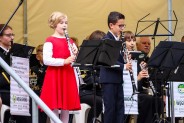 Na tle górniczej orkiesty z klarnetami stoją - dziewczynka w czerwonej sukience oraz chłopczyk w…