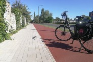 Fragment nowej ścieżki rowerowej, na której stoi czarny rower. Po prawej stronie ścieżki…