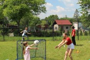 dziewczynka z wolontariuszką rzucają piłkę, w tle chłopiec skacze przez płotki