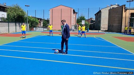 Prezydent miasta Rafał Piech stoi na środku boiska, przygotowany do kopnięcia piłki,…