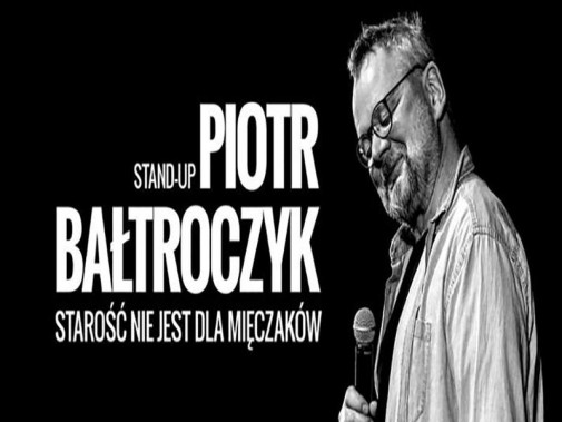 Na czarnym tle sylwetka artysty Piotra Bałtroczyka z mikrofonem w ręku, ma jasną koszulę i…