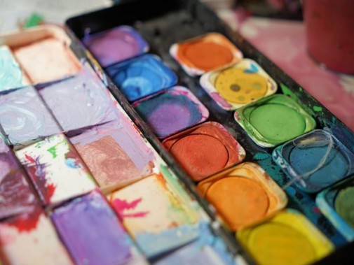 Kolorowe farby wodne w trakcie używania, w zabrudzonym farbkami pudełku.