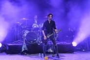 Scena Amfiteatru w niebieskim świetle. Wokalista w czarnej koszuli z gitarą śpiewa do mikrofonu. …