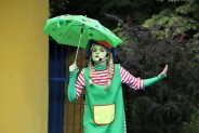 Na scenie amfiteatru aktorka grająca zielonego utopca. Trzyma w dłoniach zieloną parasolkę