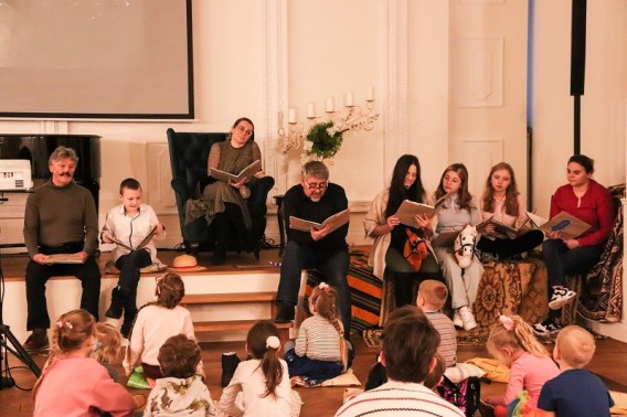 Aktorzy czytający z ksiązek bajkę na poduszkach siedzące dzieci