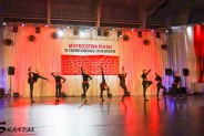 8 cheerleaderek w czarnych strojach podczas tańca na  tle flagi Mistrzostw Polski w Cheerleadingu…
