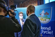 Michał Lech pozujący na ściance z logotypami miasta. Przed nim stoi kamerzysta oraz osoba…