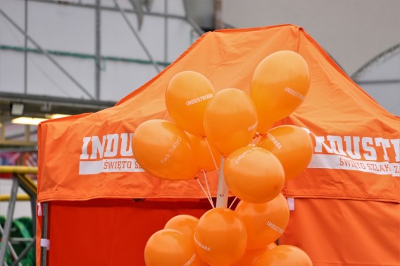 Pomarańczowy namiot informacyjny udekorowany pomarańczowymi balonami.