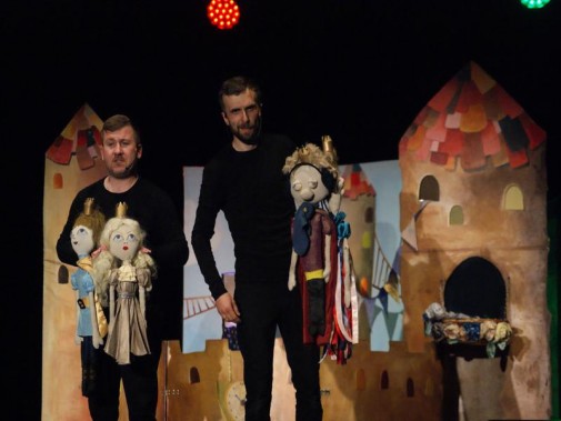 Dwoje ubranych na czarno aktorów prezentuje cztery lalki użyte w spektaklu dla dzieci. Za nimi…