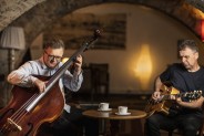 Muzycy Bohdan Lizoń i Grzegorz Piętak siedzą przy stoliku w kawiarni i grają na instrumentach