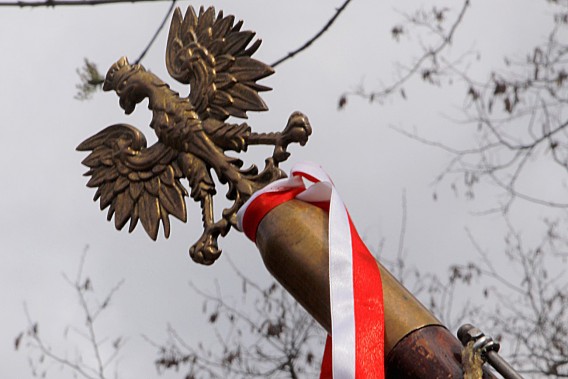 drzewiec sztandaru, zwieńczony orłem – godłem Rzeczypospolitej Polskiej, przewiązany…