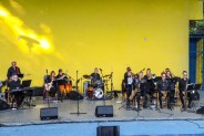 Na tle żółtej ściany amfiteatru siedzą muzycy orkiestry Siemion Band. Trwa koncert, muzycy grają…