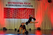 2 cheerleaderki w czarnych strojach podczas tańca na  tle flagi Mistrzostw Polski w Cheerleadingu…