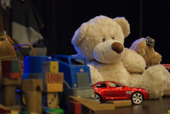 Zabawki na scenie, stanowiące element dekoracji. Miś, klocki i niebieskie oraz czerwone samochodziki