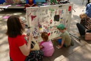 Dzieci i dorośli malują na płótnie przyczepionym do wolno stojącej metalowej ramy na kółkach