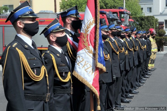 Strażacy w mundurach galowych stoją w szeregu w czasie uroczystej zbiórki z okazji Dnia Strażaka