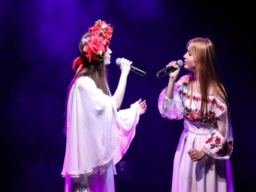 Dwie ubrane na biało dziewczyny w sukniach stylizowanych na ludowe ukraińskie. Jedna ma na głowie…