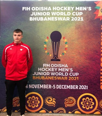 Zawodnik podczas na tle plakatu Mistrzostw Świata U21 w hokeju na trawie