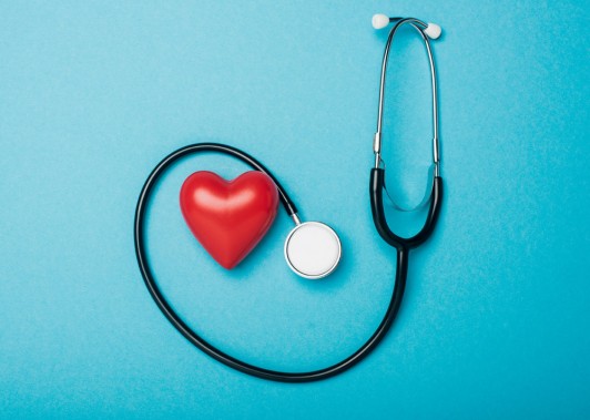 Stetoskop owinięty wokół czwerwonego serca na jasnym błękitnym tle