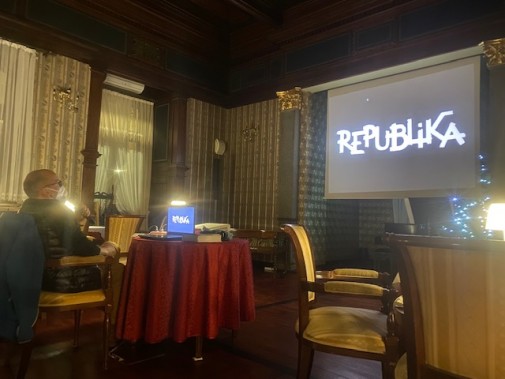 Bartłomiej Gruchlik siedzi na fotelu twarzą do ekranu, na którym widnieje logo zespołu Republika.
