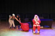 Siedzący Mikołaj i aktorki podkradające worek z prezentami podczas spektaklu w SCK Parku Tradycji