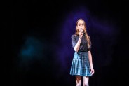 Na zdjęciu wokalistka z sekcji wokalnej działającej w SCK Bytków. Ma na sobie niebieską sukienkę.…