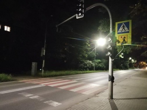 Przejście dla pieszych nocą, obok niego znajduje się sygnalizacja świetlna, znaki drogowe oraz…