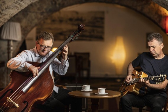 Na zdjęciu muzycy Bohdan Lizoń i Grzegorz Piętak siedzą w kawiarni i grają na instrumentach