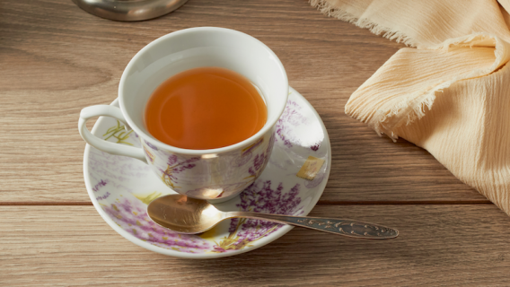 Biała filiżanka wypełniona herbatą na drewnianym stole