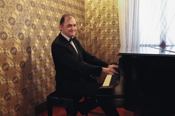 Uśmiechnięty mężczyzna w średnim wieku w czarnym garniturze, białej koszuli grający na fortepianie