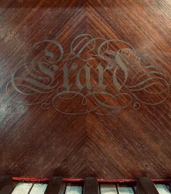Zdjęcie przedstawia drewniany front fortepianu, widoczny jest napis „Erard”