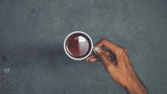 Grafika przedstawia dłoń trzymającą białą filiżankę z herbatą na szarym tle