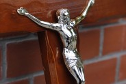 Fragment drewnianego krzyża nagrobnego z figurą Jezusa ukrzyżowanego, oparty o ceglaną ścianę…