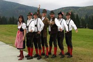 zespół Tyrolia Band stojący w bawarskich strojach na tle gór. Sześciu mężczyzn oraz jedna kobieta.