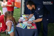 Policjant pokazuje dziewczynce kolorowe książeczki o bezpieczeństwie