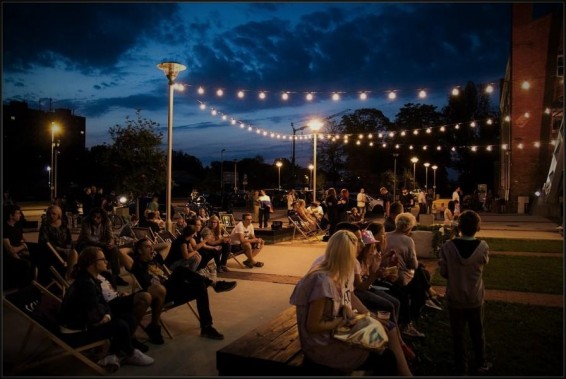 Na zdjęciu koncert z cyklu Chill Time. Ludzie siedzą na leżakach i ławkach słuchając muzyki. Jest…