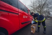 Strażak z siemianowickiej OSP sięga po maseczki, stojąc przy czerwonym samochodzie strażackim.