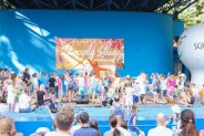 Widok ogólny na scenę amfiteatru, gdzie duża grupa dzieci bawi się wspólnie z aktorami