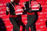 2 cheerleaderki w czarnych strojach z medalami, dyplomami i pucharami