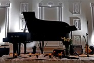 Czarny fortepian w białej sali o podświetlanych ścianach.